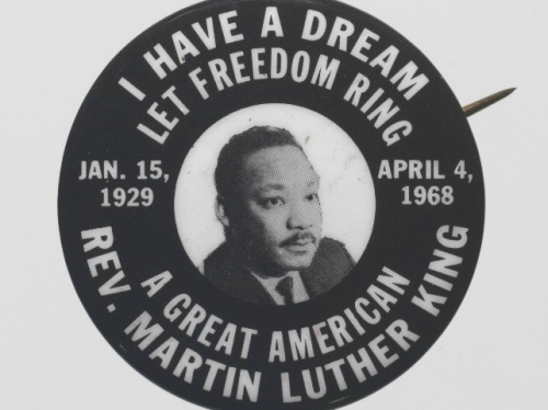 Photograph of black and white pinback button with image of Martin Luther King Jr.s face in center surrounded by quotes.