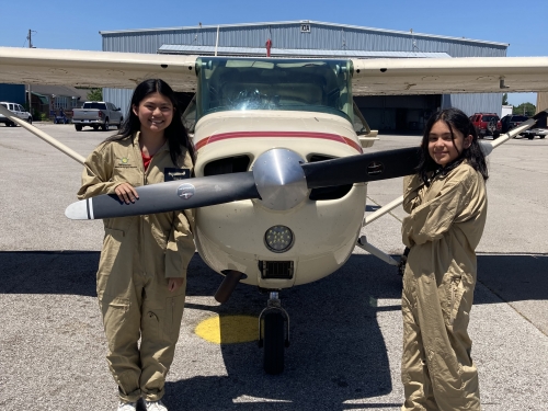 Two teenagers stand outside next to small plane and its propellers