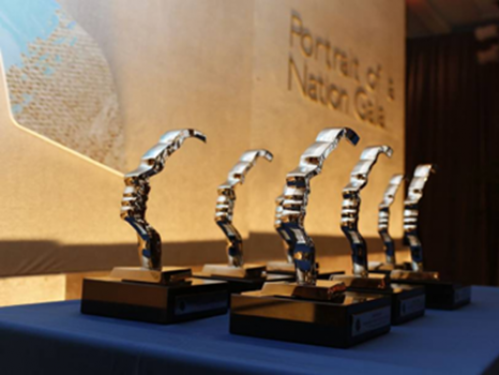 A group of awards with silver hand sculpture and wood base sit on a podium.