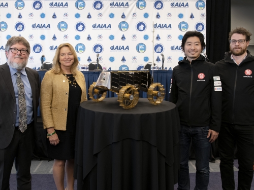 Four people stand next to a table topped with rover