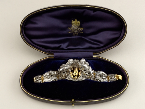 Ornate cupid bracelet in an open case lined with dark satin fabric.