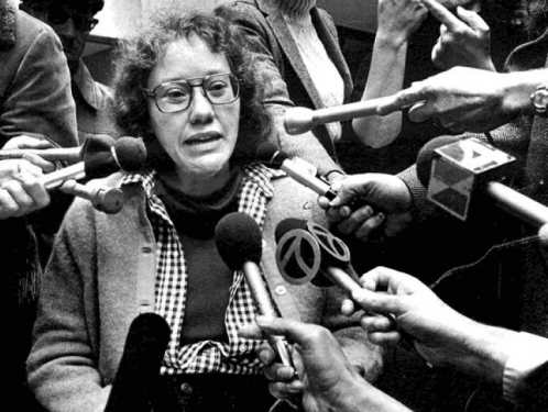 Kitty Cone with reporters holding microphones in her direction.