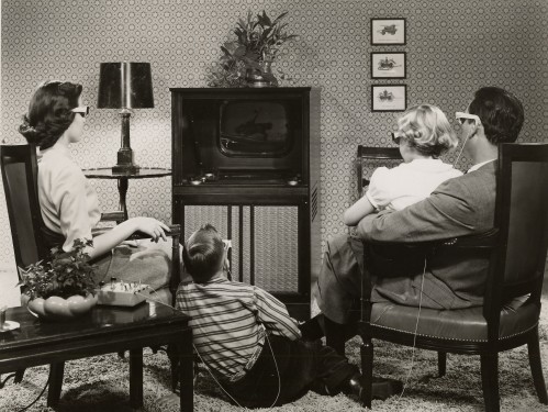 A family sits watching TV in a black and white photograph.