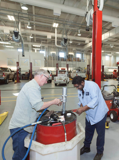 Two men working together in a shop with vehicles around them