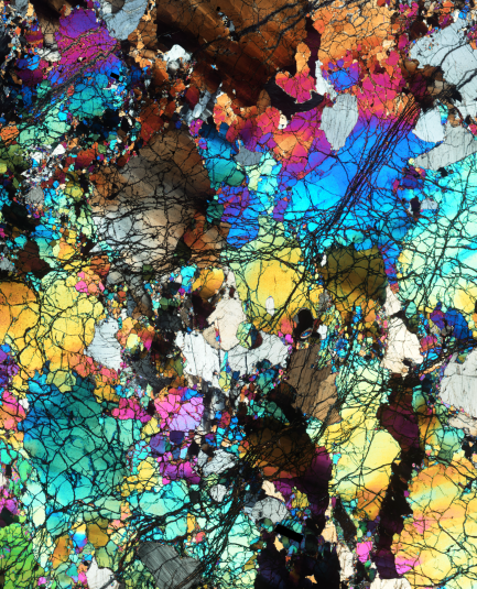 Cross-section of microscopic slice of rock with vibrant colors--white, blue, pink, orange, brown, green.