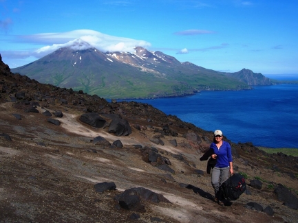Woman walks on side of volcano overlooking a body of water