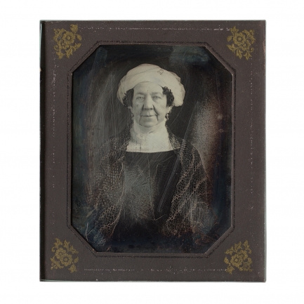Black and white image of woman wearing dark dress and white headwrap in a small frame.