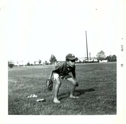 Young boy crouches in a field of grass with a baseball mitt in hand
