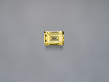 Close-up of a singular yellow diamond, emerald cut, against a plain gray background.