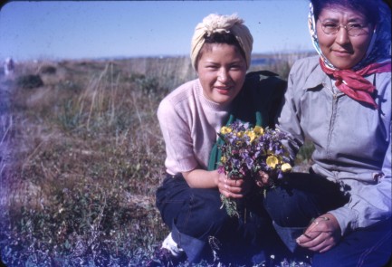Vintage photo of women kneeling in a field holding flowers.
