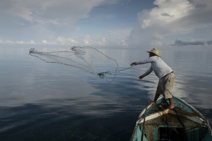 Fisherman casts seine net from small boat
