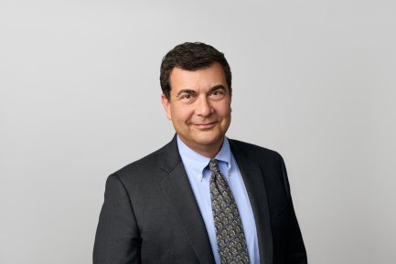 Man with short dark hair smiles with mouth closed, wearing a dark suit.