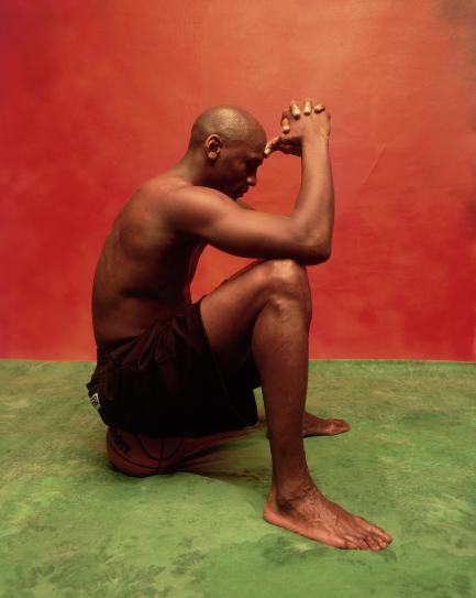 Black man sitting against red wall on green floor
