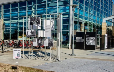 Section of a fence displays artwork in fromt of a building