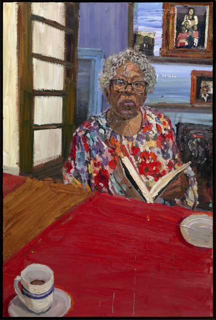 Woman wearing glasses with short white hair sits in a dining room reading a book.