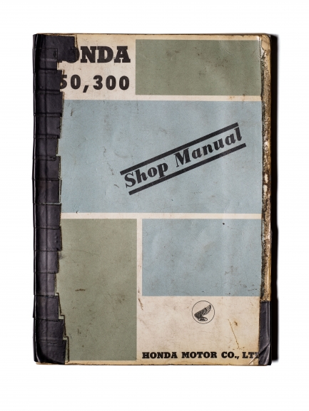 Bound papers with blocks of green and blue and large stamped text saying Shop Manual.