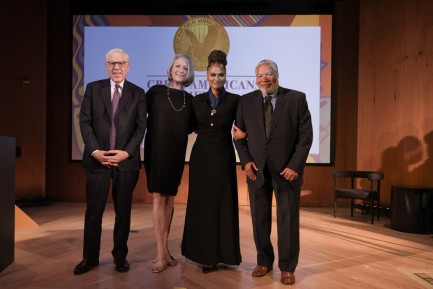 Two men and two women in evening wear pose for a photo on a stage.