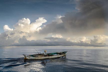 Lone fisherman in small boat against dramatic sky