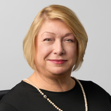 Woman with blonde bob wearing a black top, sitting in black wheelchair, smiles toward camera