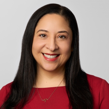 Woman with long black hair in a red dress smiles for a headshot.