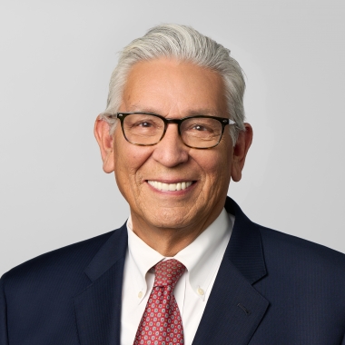 Man in a dark suit and red tie, wearing glasses, smiles for a headshot.