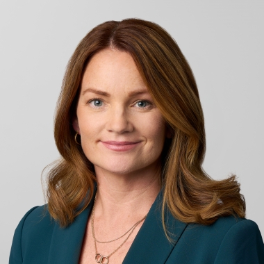 Woman with long, dark red hair in a white blouse and deep blue blazer smiles for a headshot.