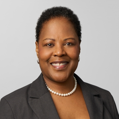 Woman in a dark blazer and pearls smiles toward camera