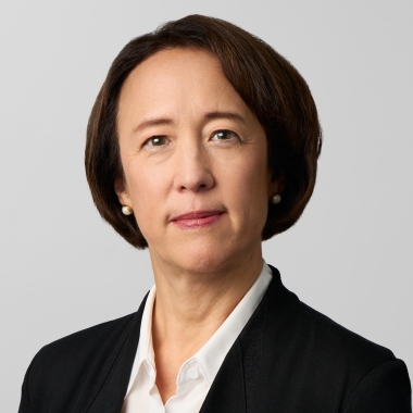 Woman with chin-length black hair in a dark blazer and white button-up stands sits for a portrait.
