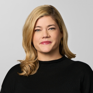 Woman with curled blonde hair wearing a black blouse smiles for a headshot.
