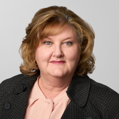 Woman with shoulder-length, curled strawberry blonde hair wearing a black blazer smiles for headshot
