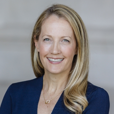 Headshot of a woman with medium-length blonde hair, smiling, wearing a blue dress.