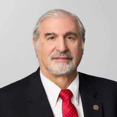 Man in a dark suit with a bright red tie smiles for a headshot.