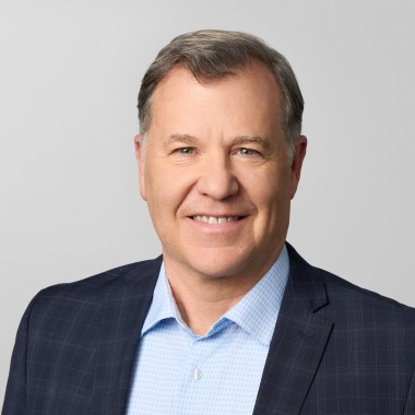Man with short hair wearing a blue button down and black blazer smiles for a headshot.
