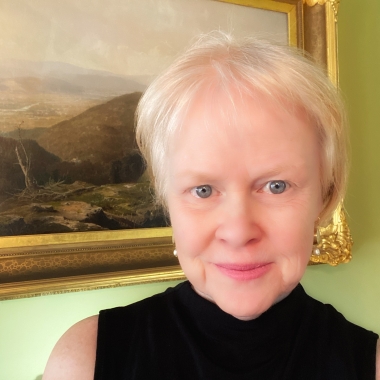 Woman with short hair, blue eyes and a sleeveless, blakc turtleneck smiles toward camera.
