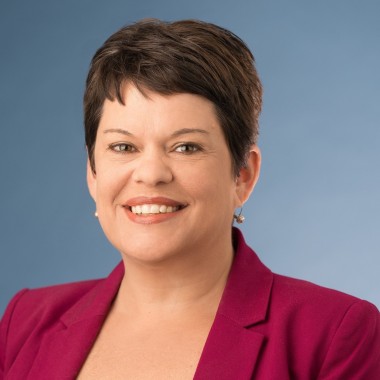 Headshot of a woman with a brown pixie cut, smiling, wearing a red blazer.